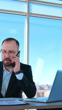 Ofiste telefonla konuşan kendine güvenen bir iş adamı. Bir patronun portresi masada oturuyor ve telefonda iş sorunları ile uğraşıyor. Dikey video