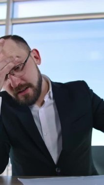 Ofiste oturan bir iş adamının portresi. Takım elbiseli ve gözlüklü bir girişimci pencere önünde iş hakkında konuşuyor. Dikey video