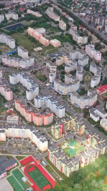 Yeşil bitkileri olan şehir manzarası. Modern şehir bölgesinde yeni bir yerleşim yerinin yüksek katlı evleri. Hava görüntüsü. Dikey video