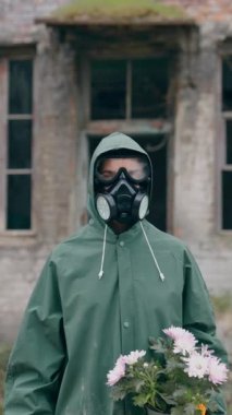 Mahvolmuş binanın arka planında elinde çiçeklerle hayatta kalan biri. Kimyasal güvenlik kıyafeti giyen ve elinde çiçeklerle terk edilmiş bir yerde duran biri. Kimyasal saldırı. Dikey video
