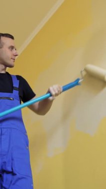 Odada boyama duvarı var. Uzun bir çubukta paten fırçasıyla dairede tadilat yapan profesyonel bir işçi. Aşağıdan bak. Dikey video