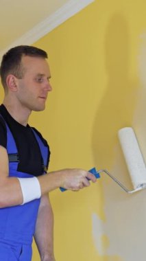 Profesyonel ressam duvarları tekerlekli fırçayla boyar. Mavi tulumlu işçi, tadilat yapıyor ve daireyi geliştiriyor. Tamir ve dekorasyon. Dikey video