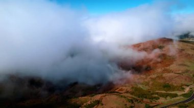 Kayalık arazi boyunca bir otoyol gider. Dağın tepelerini gizleyen kalın beyaz bulutlar. Madeira manzarası, Portekiz.