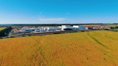 Sarı tarım alanının üzerinden uçarak büyük bir fabrikaya yaklaşıyorlar. İş konsepti. Arkaplanda mavi gökyüzü.