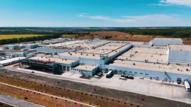 Modern endüstriyel bir fabrikanın geniş bir bölgesi, havadan bakıldığında. Ormanlar ve tarlalar arka planda.