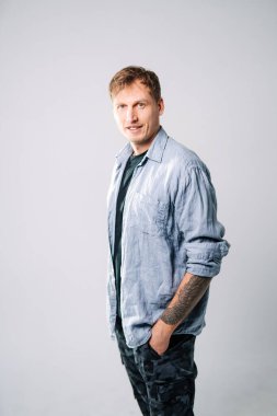 Açık tişörtlü ve siyah pantolonlu adam. Adam rahat bir poz verirken rahat bir şekilde gülümsüyor tarafsız bir arkaplana karşı, günlük giysiler giyiyor..