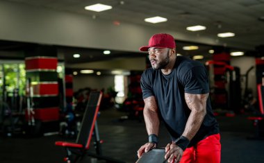 Adanmış sporcu, yoğun bir spor salonunda ağırlık kaldırır. Odaklanmış bir adam hareketli bir spor salonunda ağırlıklarla egzersiz yapar. Kararlılık ve güç gösterisi yapar..