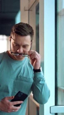 Pencere çerçevesine yaslanmış kendine güvenen yakışıklı bir adam. Orta yaşlı, gülümseyen beyaz bir adam gözlük takıp kameraya bakıyor. Kapatın. Dikey video