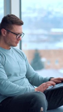 Gözlüklü meşgul bir adam dizüstü bilgisayarına dikkatle bakıyor. Freelancer bir anlığına pencereden dışarı bakarken dikkatini dağıtıyor. Dikey video