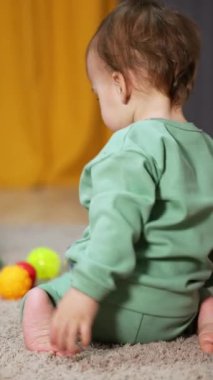 Aktif beyaz çocuk içeride yerde oyuncaklarla oynuyordu. Tatlı çocuk yeşil plastik bir simit alıp kameraya atıyor. Dikey video