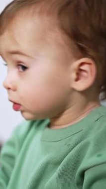 Sevimli bebek kameraya şaşkınlıkla bakıyor. Kapatın. Çocuk yerde, etrafında oyuncaklarla oturuyor. Arkaplan bulanık. Dikey video