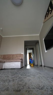 Sevimli erkek bebek odaya koşup oyuncak arabasını itiyor. Aktif çocuk evde oyuncaklarla oynuyor. Düşük açı. Dikey video.