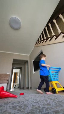 Neşeli çocuk oyuncak piramit detaylarını yerden topluyor. Çocuk oyuncaklarını arabaya koyar ve mutlu adımlarla yürür. Düşük açı. Dikey video.