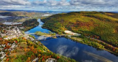 Ortasında küçük bir ada ve üzerinde köprü olan mavi bir nehre yaklaşıyoruz. Vermont, New England, ABD 'nin bulutlu gökyüzü altındaki manzarası.