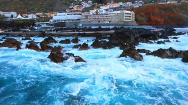 Dalgalar, Portekiz 'in Madeira kıyısında sudan çıkan birden fazla kayadan su sıçratır. Deniz manzarasının üstündeki kıyıda drone görüntüleri..