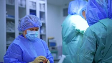 Dişi hemşire neşteri kanla temizliyor. Koruyucu miğferli doktorlar travma ameliyatı gerçekleştiriyor..