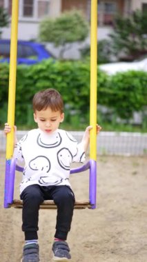 Salıncakta sallanan Kafkasyalı çocuk. Annemin eli salıncağı itiyor. Açık hava zaman harcaması. Dikey video.