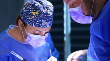 Kelebekli şapka takan kadın doktor ameliyat yapıyor. Cerrah elektrikli alet ve metal alet kullanıyor. Kapat..