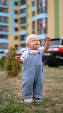 Kot pantolon giyen güzel sarışın beyaz erkek bebek dışarıda duruyor. Toddler bir meşe palamudu gösteriyor ve ailesine veriyor. Çocuk ağzına çam kozalağı koymak istiyor ama fikrini değiştiriyor. Dikey video.