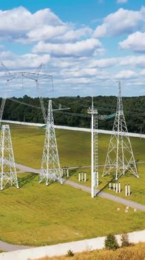 Yeşil alanda yüksek voltajlı çelik sütunlar. Gün ışığında güç iletim hatları. Yaz günü beyaz elektrik kuleleri. Dikey video
