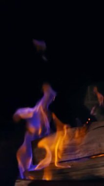 Taş şöminede yanan mavi ve sarı ateş. Tahta kütükler karanlıkta yanıyor. Sıcak ve sıcak bir atmosfer. Dikey video