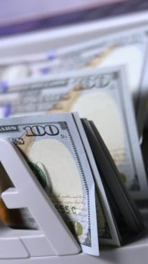 Bankada yüz dolarlık banknotları saymak. Modern bir elektronik para sayma makinesinde finansal işlem. Kağıt para saymak için otomatik ekipman. Dikey video