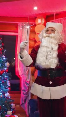 Mutlu Noel Baba 'lar Noel süslemeli odada. Noel Baba, kırmızı kostümlü sakallı, Noel ağacının yanında duruyor. Elinde Noel ışıkları olan otantik Noel Baba. Dikey video