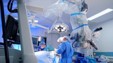 Modern ameliyat odasındaki kürsüde mikroskop var. Bir grup doktor arka planda ameliyat yapıyor..