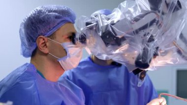 Maskeli beyaz cerrah mikroskoba dikkatlice bakıyor. Doktor beyin cerrahisinde aletleri uyguluyor. Yan görünüm.