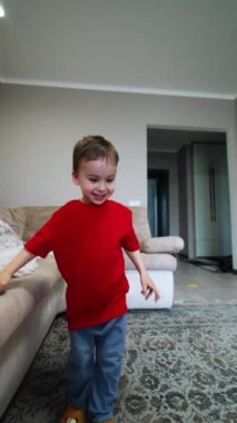 Mutlu çocuk evdeki kanepede takla atıyor. Enerjik erkek bebek kanepede ayaklarını sallıyor. Dikey video.