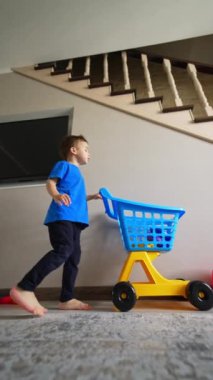 Çıplak ayaklı beyaz çocuk oyuncaklarını el arabasına topluyor. Düşük açı. Disiplin kavramı. Dikey video.