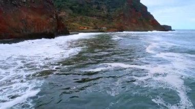 Köpüklü dalgalar siyah sahilde yuvarlanır. Portekiz, Madeira 'nın kayalık kıyılarının yakınındaki su üzerinde insansız hava aracı görüntüleri..