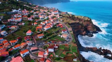 Mavi okyanus yakınlarındaki kayaların üzerinde turuncu çatıları olan çok sayıda kulübe. Portekiz, Madeira 'daki şehrin panoramasının üstündeki insansız hava aracı görüntüleri..
