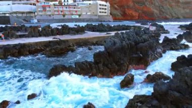 Portekiz 'in Madeira kıyısındaki kayaların üzerinden okyanus dalgaları süzülür. Rıhtımdaki ve kayalık sahildeki görüntüler.