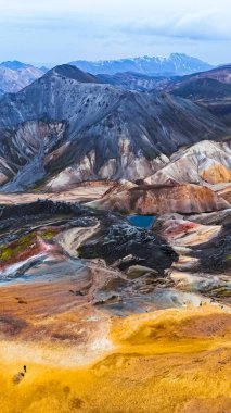 İzlanda 'daki canlı dağlar ve gayzerler. Canlı jeotermal manzaraları ve İzlanda 'nın çarpıcı dağlarında bulutlu bir gökyüzünün altındaki engebeli dağları keşfedin..