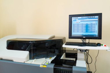 Bilgisayarlı ofis baskı makinesi. Yüksek teknolojili bir matbaa makinesi bir ofiste bilgisayarın yanında duruyor, mesai saatlerinde belge üretimine hazır..