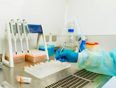Laboratuvardaki bilim adamı pipetleri kullanıyor. Eldivenli bir bilim adamı, temiz bir laboratuvar ortamında sıvı örnekleri taşımak için pipetleri dikkatlice kullanıyor..