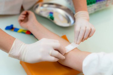 Doktorlar, tedavi sonrası çocuğun kolunu bandajlıyorlar. Bir tıp uzmanı, klinikte küçük bir tedavi sonrası çocuğun koluna bandaj uygular..