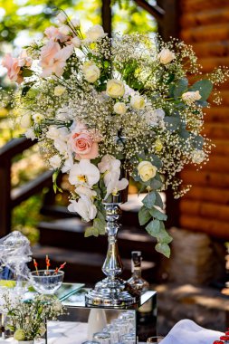 Açık hava düğününde şıklık açar. Açık havada bir düğünde, güller, orkideler ve narin yeşilliklerin yer aldığı çarpıcı bir çiçek süsü dimdik ayakta duruyor..