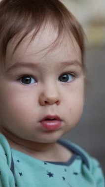 Sevimli, gri gözlü, tapılası tombul yanaklı çocuk kameraya bakıyor. Bebek elindeki kabloya bakıyor. Kapatın. Arkaplan bulanık. Dikey video