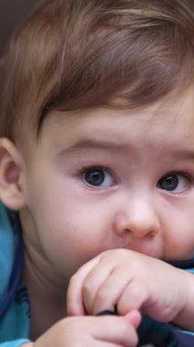 Komik beyaz çocuk yerde yatıp siyah danteli çiğniyor. Güzel bebek yanındaki parlak oyuncak arabaya ulaşıyor. Kapatın. Dikey video