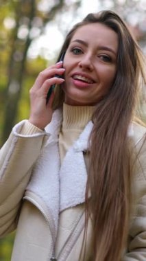 Açık havada gülümseyen çekici bir esmer. Kadın kameraya bakıp telefonunu kulağına tutarak saçına dokunuyor. Dikey video