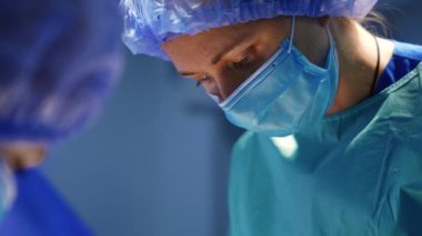 Ameliyat sırasında zaman zaman kaşlarını çatan kadın cerrahın yüzü. Maskeli ve şapkalı doktorun ameliyat yaparken çekilmiş portresi..