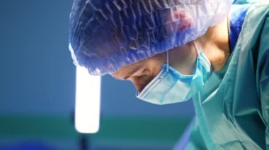 Kadın doktor hastaya doğru eğildi. Hastayı ameliyat eden maskeli ve şapkalı cerrahın yan görünümü..