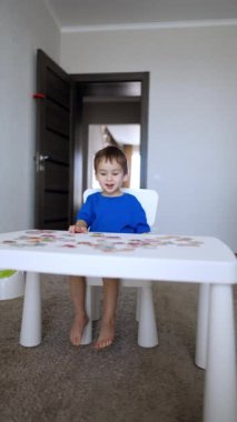 Sevimli gülümseyen bebek masada bulmacalarla oynuyor. Sevimli çocuk oyunla ilgileniyor. Dikey video.