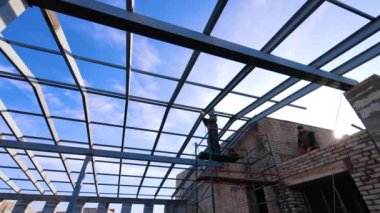 Metal kaynak yapan adam, geleceğin çatısı için çerçeve yapmayı reddediyor. İnşaatta çalışan inşaatçıların düşük açılı görüntüsü.