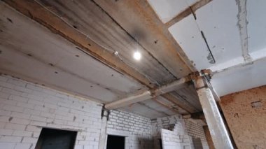 Eski püskü tavanda bir kablo ve ampul açık kalmış. Binanın tavanı yeniden yapılandırılırken alçak açı görüntüsü.