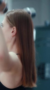 Siyah bluzlu, sıska bir kadın spor salonunda elleri ve dambıllarıyla egzersiz yapıyor. Spor malzemeleri. Bulanık Arkaplan