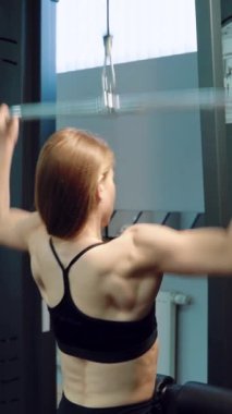 Siyah bluzlu güçlü bir kadın spor salonunda dikey çekiş yapıyor. Yakın plan.
