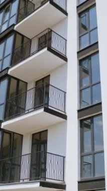 Gökyüzü arkaplanındaki apartman blokları. Pencereleri ve büyük balkonları olan modern bir apartman dairesi. Kamera yükseliyor. Dikey video